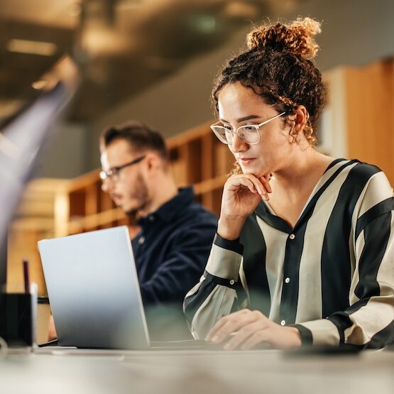 Portrait of Enthusiastic Hispanic Young Woman Working on Computer in a Modern Bright Office. Confident Human Resources Agent Smiling Happily While Collaborating Online with Colleagues.